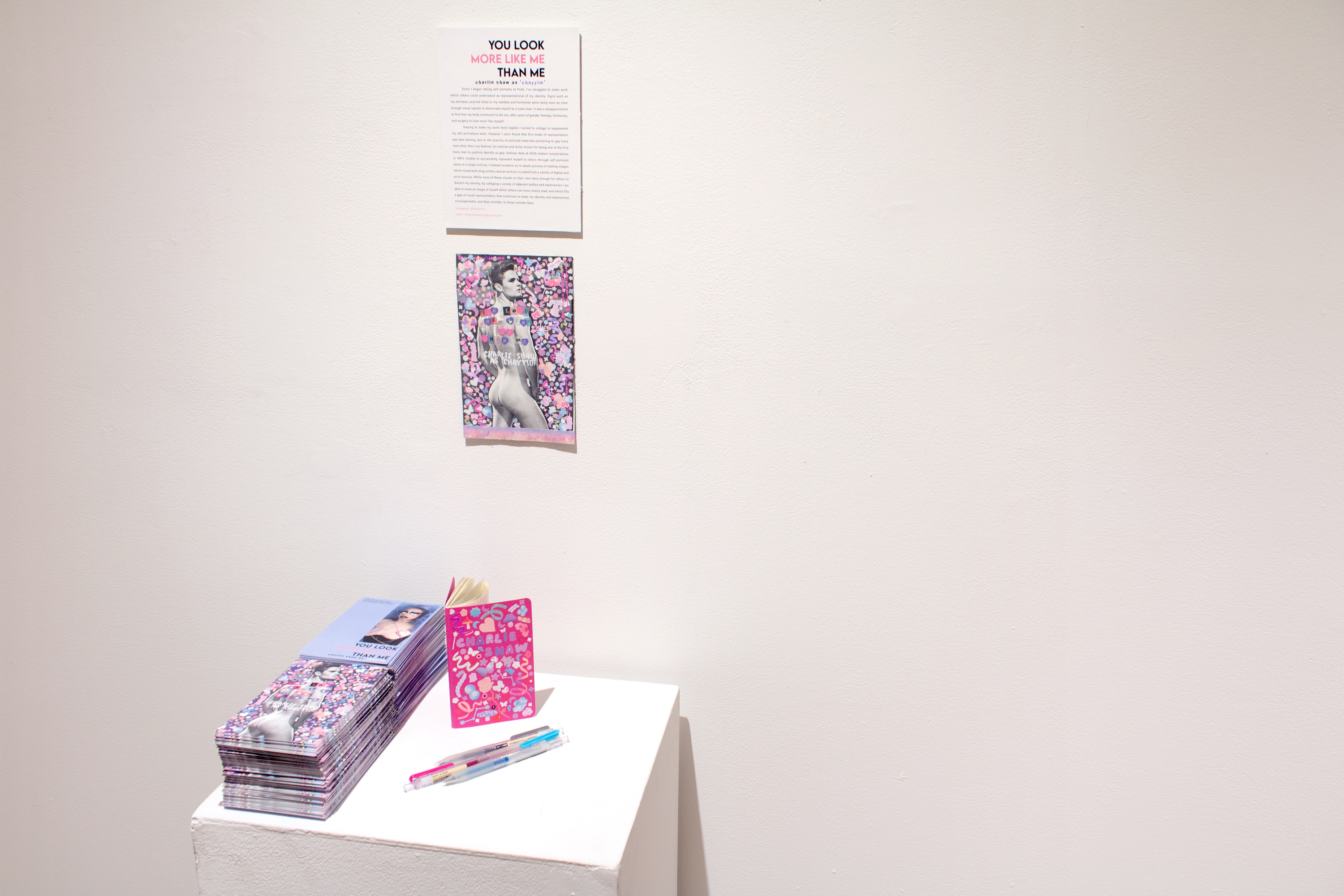 close-up of the podium with postcards, visitor's notebooks, and artist statment, all in shades of pink, purple, and blue